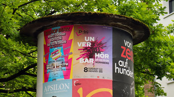 Litfassäule Plakat Unverhörbar neben anderen Plakaten