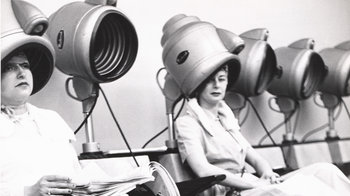 Photo Archiv Schweitzer: 2 Frauen unter Trockenhauben, spielendes Kind