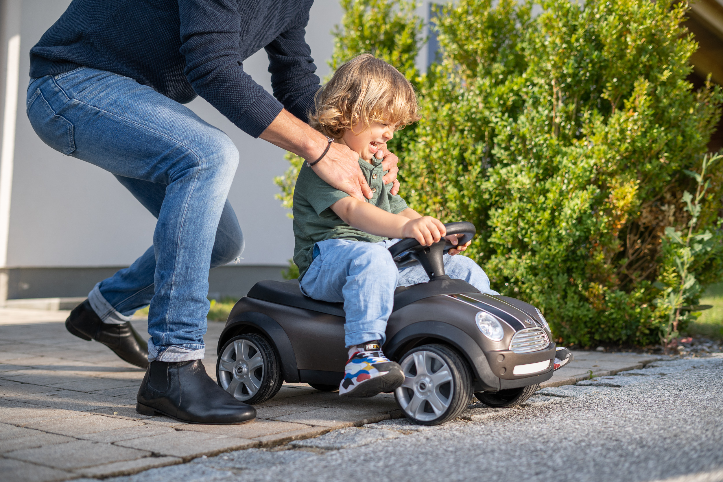 Kleiner Junge auf Boby Car wird von Erwachsenem geschoben